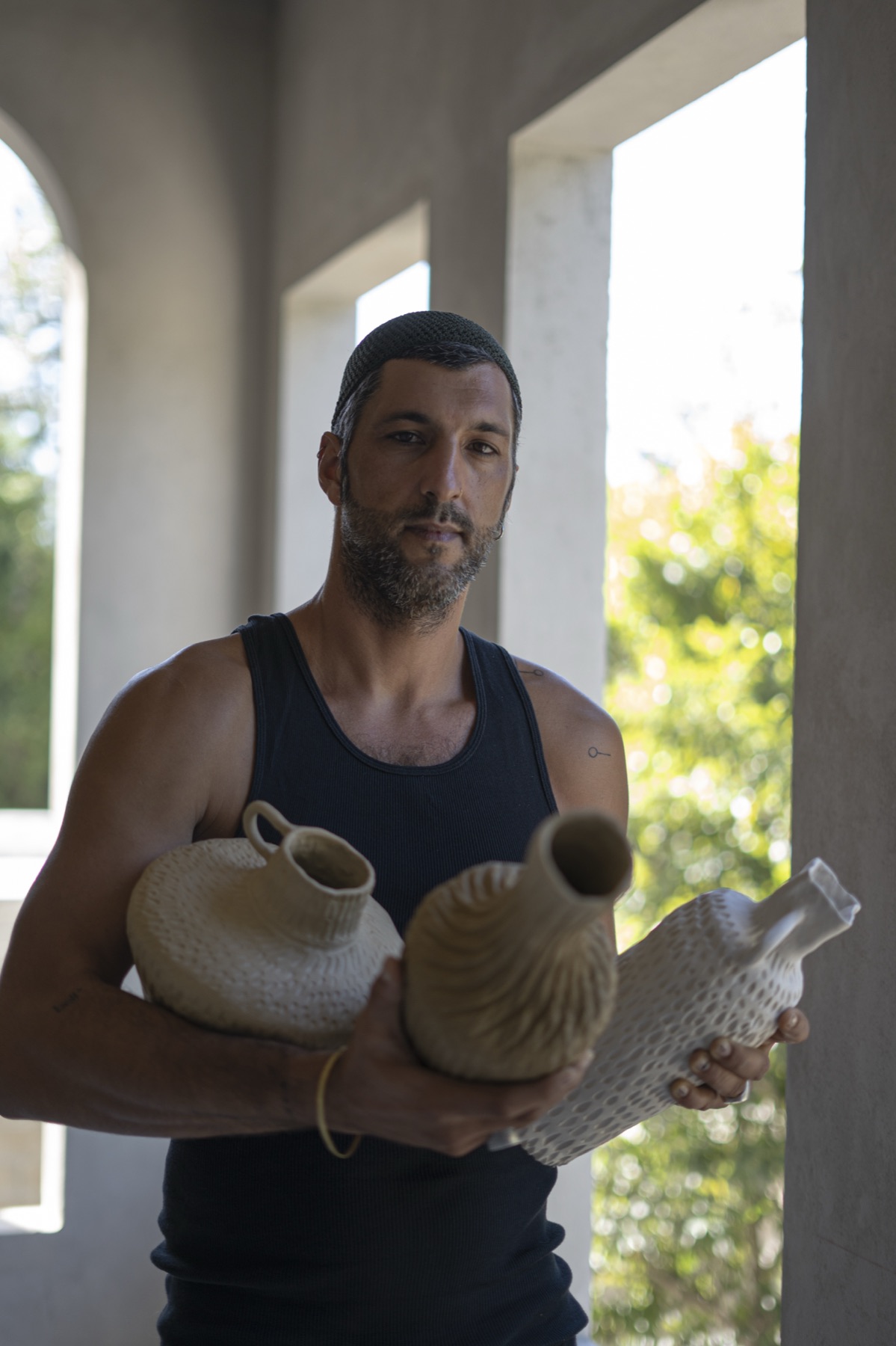 The maker standing in a colonnade, a vessel cradled in each arm.