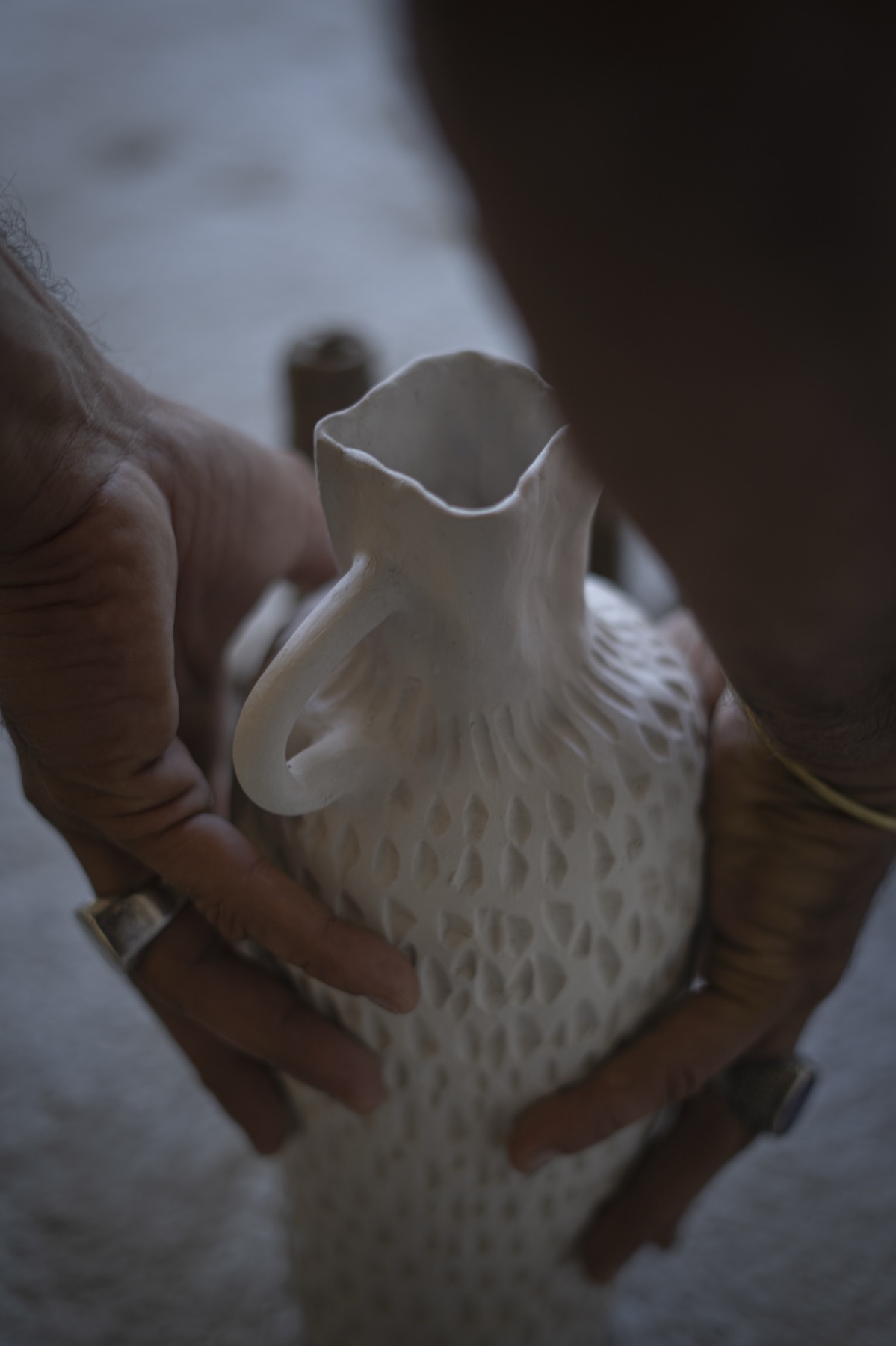 Two hands cradling a white vessel with a scalloped rim and a dotted surface.