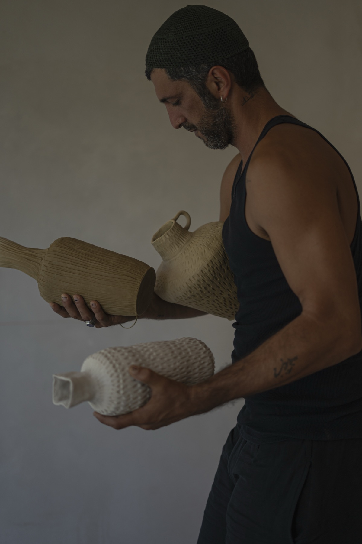 The maker holding a large ribbed vessel against his chest, a smaller one in his hand.