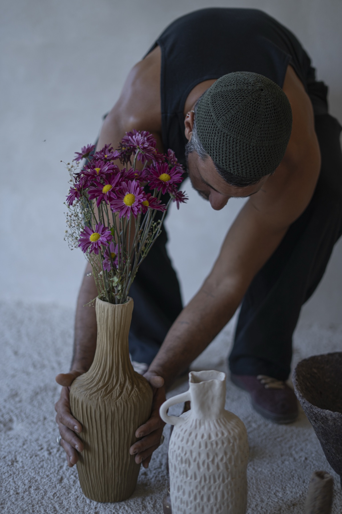 The maker leaning down to arrange magenta flowers in a tall ribbed vase.