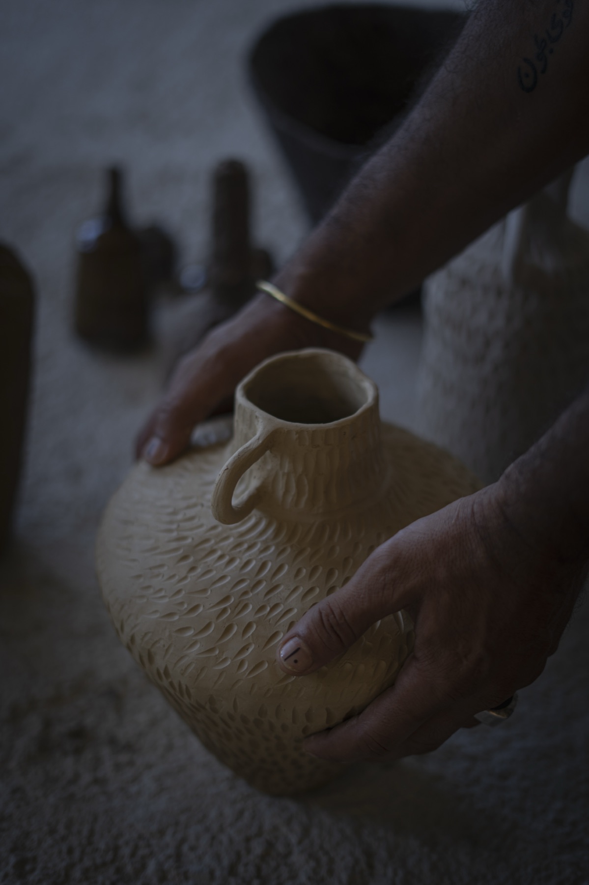 Hands turning a round, textured jug in the light.