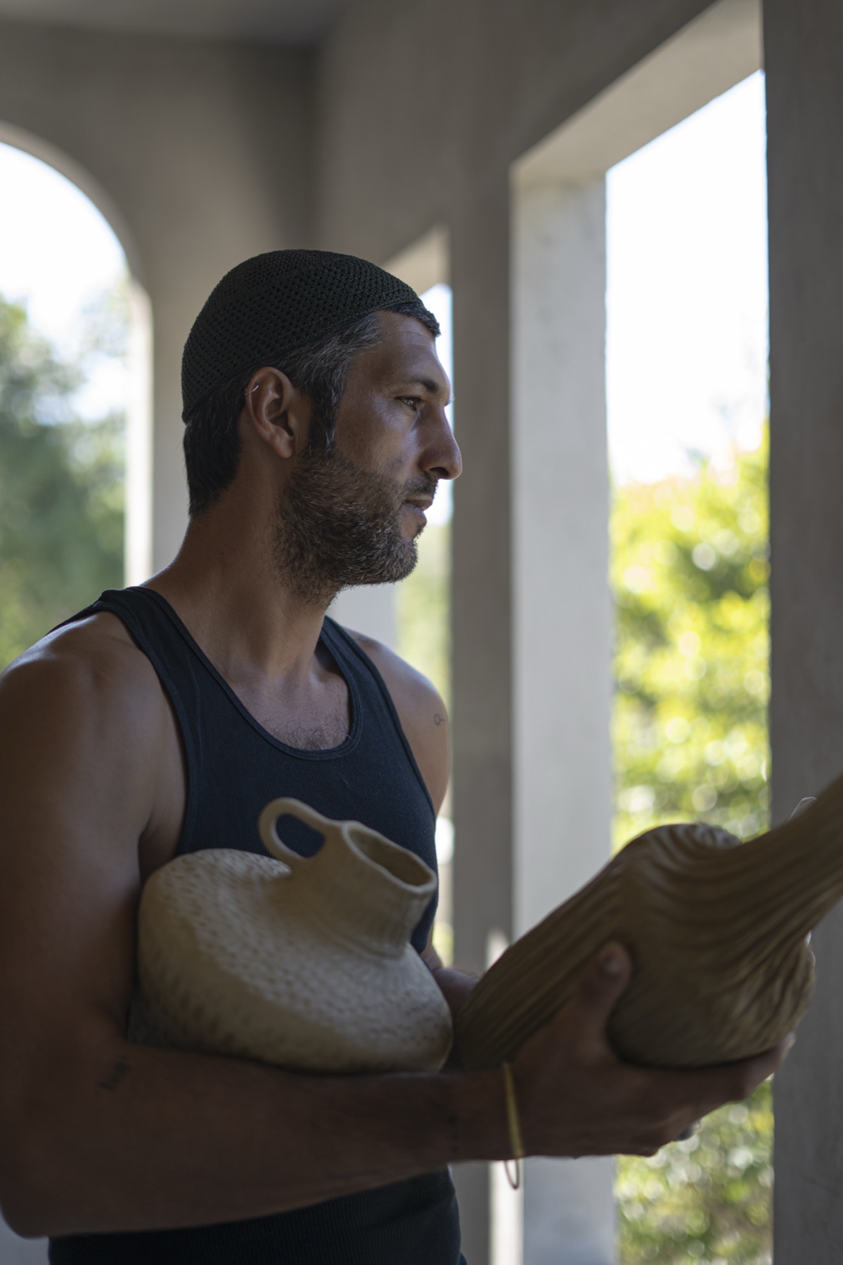 The maker in profile at a window, vessels held in both arms.