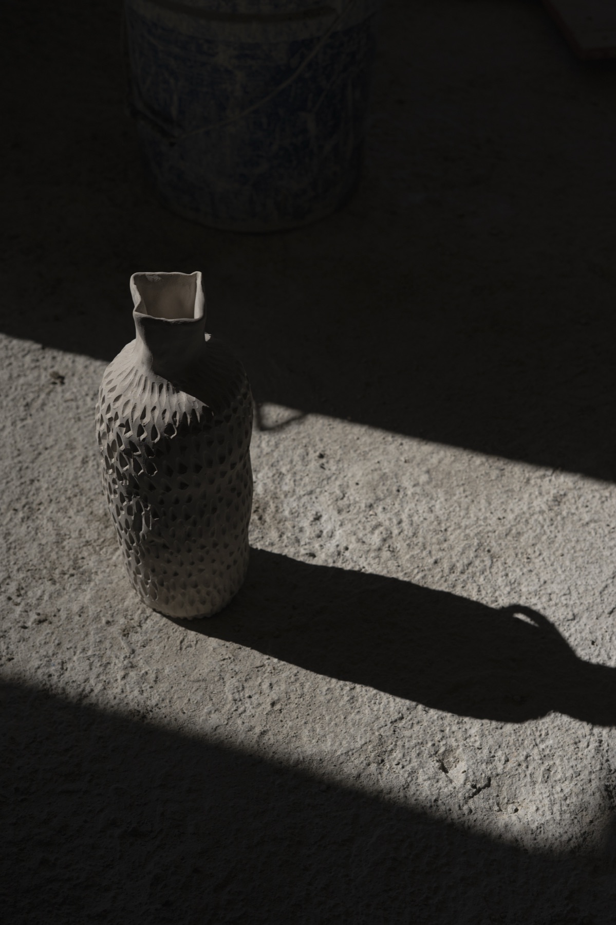A pale speckled bottle on sunlit stone, its shadow stretched long beside it.