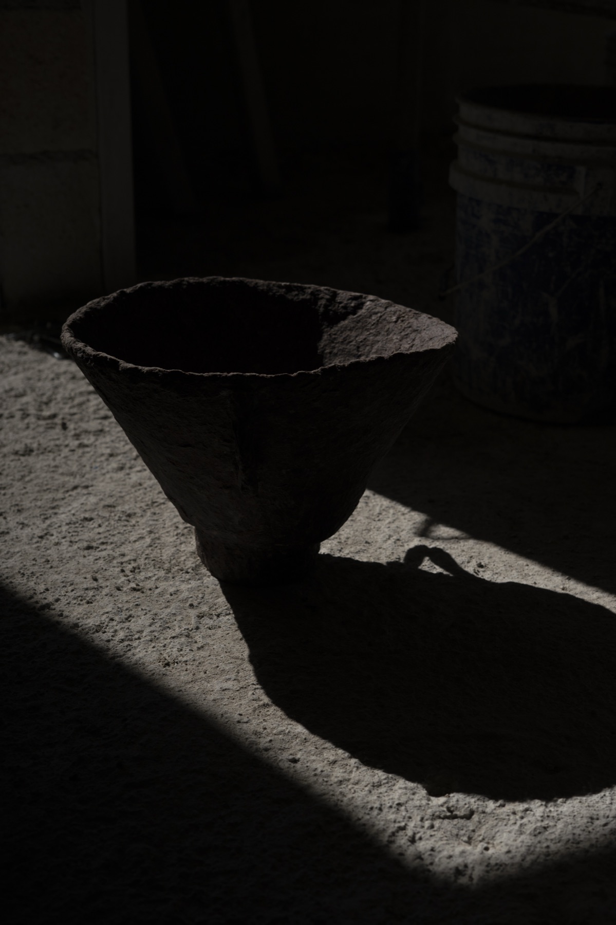 A wide conical bowl at the edge of the light, half in shadow.