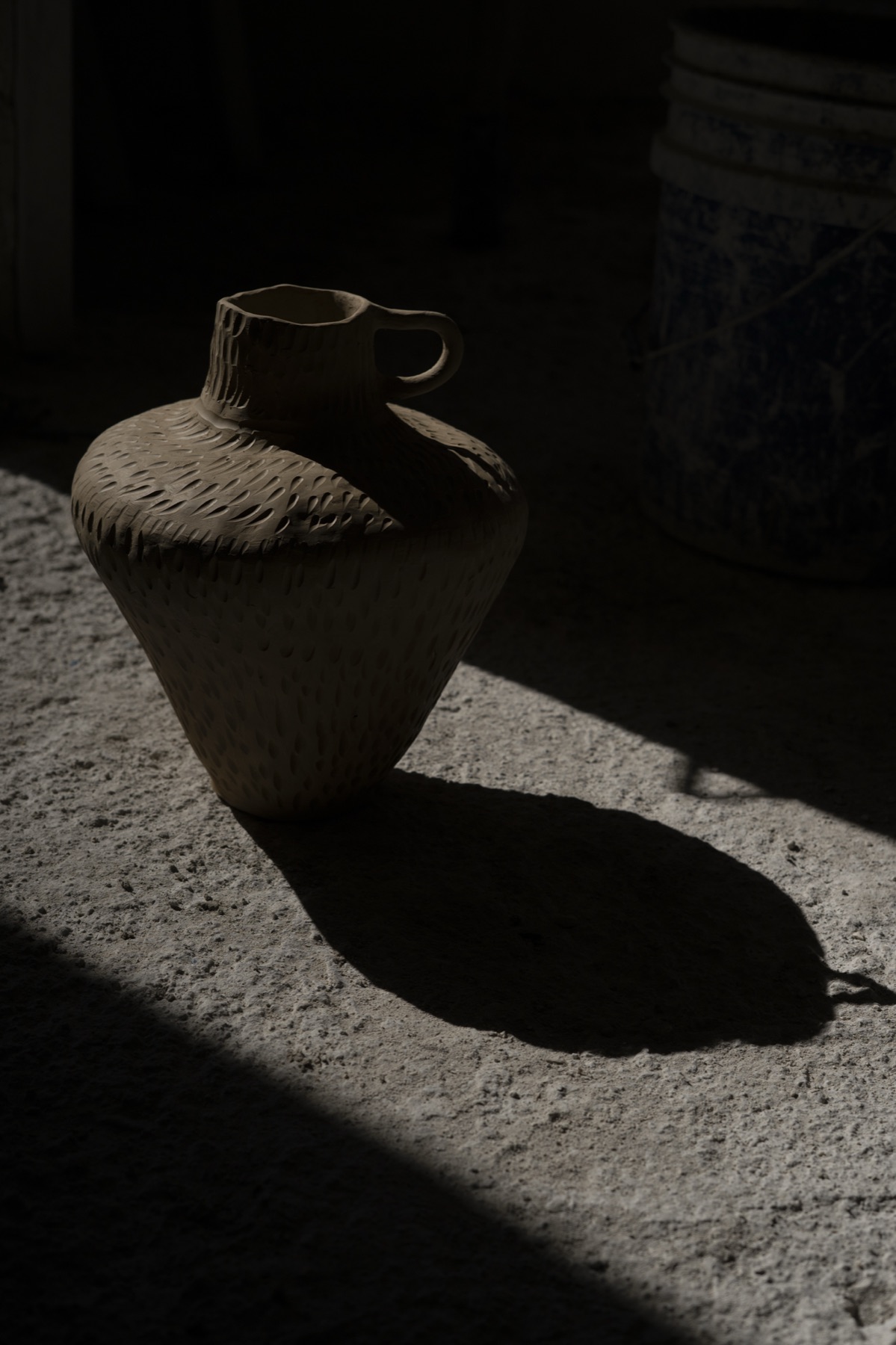 A round-bellied vessel with two handles, lit from the side, shadow across the stone.