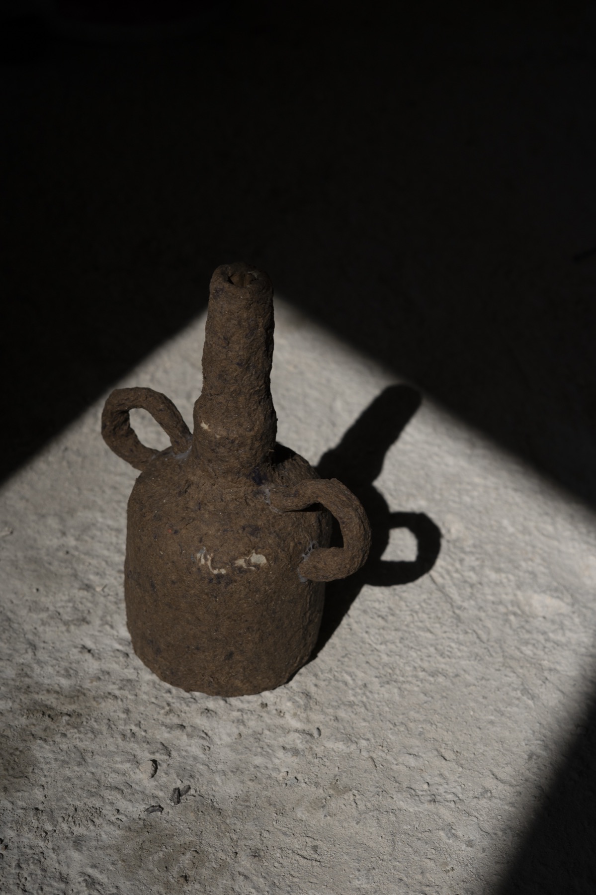 A small spouted vessel with looped handles on a lit ledge.