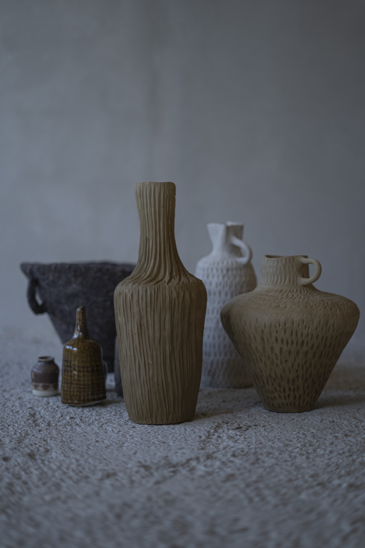 Finished vessels gathered on a plaster ledge — ribbed, dotted and smooth forms side by side.