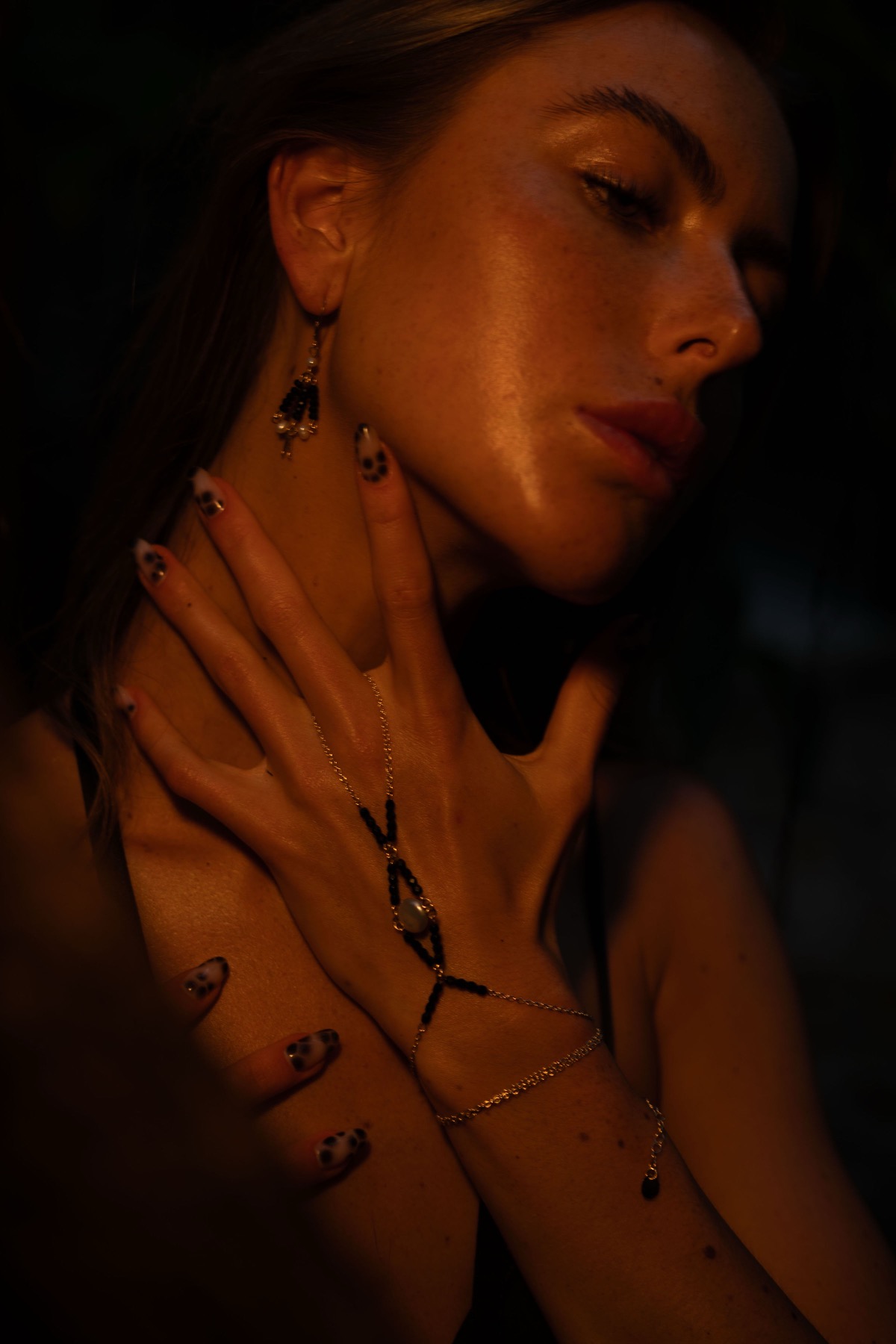 A gold hand chain with black stones laid across a woman's collarbone, her hand at her neck.
