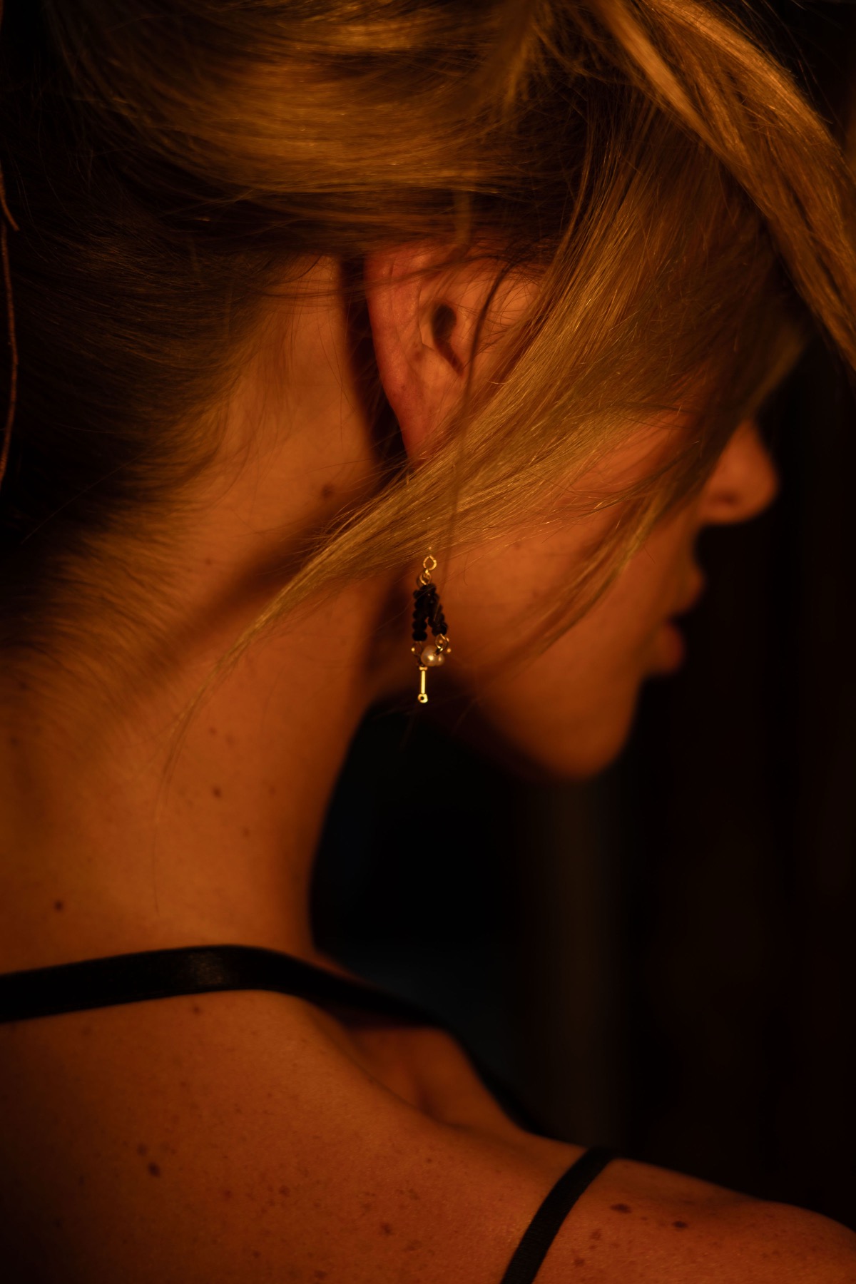 A gold and black drop earring hangs free against the back of a woman's neck and shoulder.