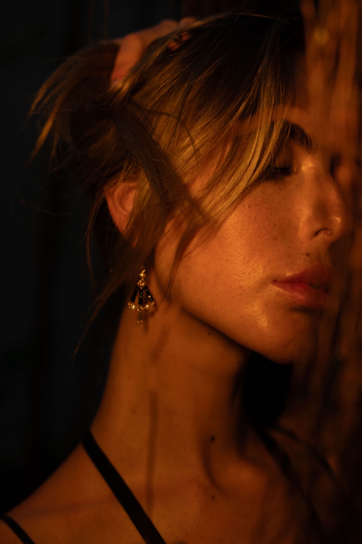 Profile of a woman with her hair up wearing an ornate gold drop earring, warm rim light.
