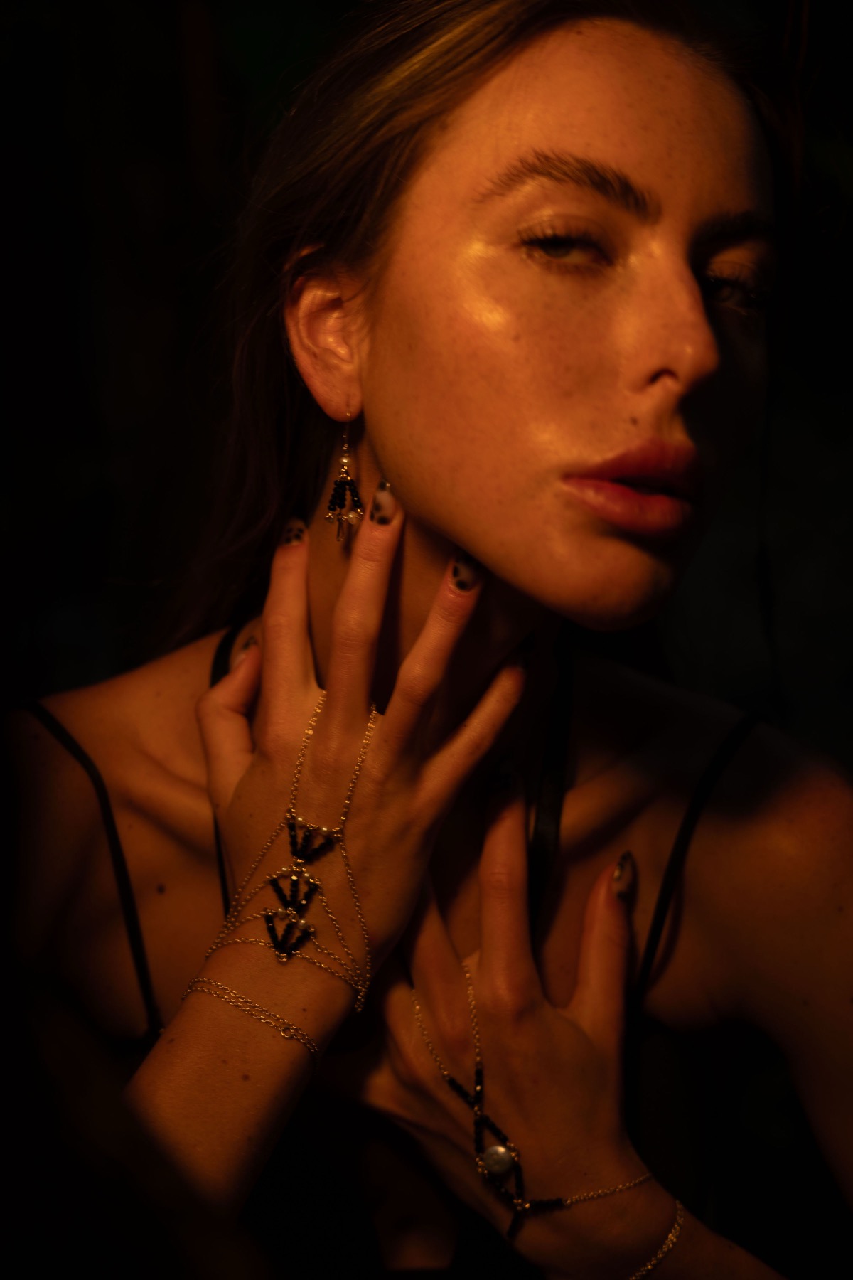 Both hands at a woman's throat, gold chain jewellery across the backs of her fingers.