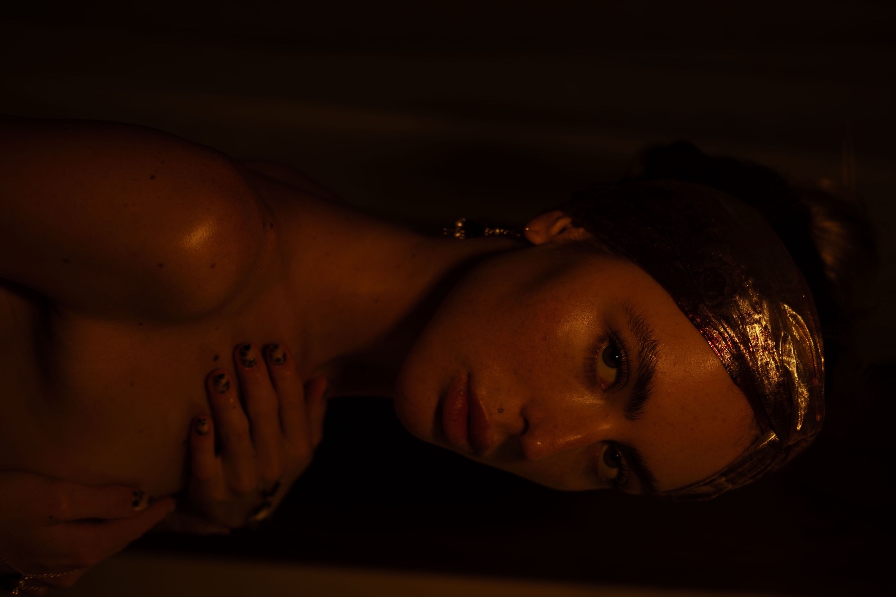 A woman lies with her head turned to camera, a gold brocade headwrap across her brow.