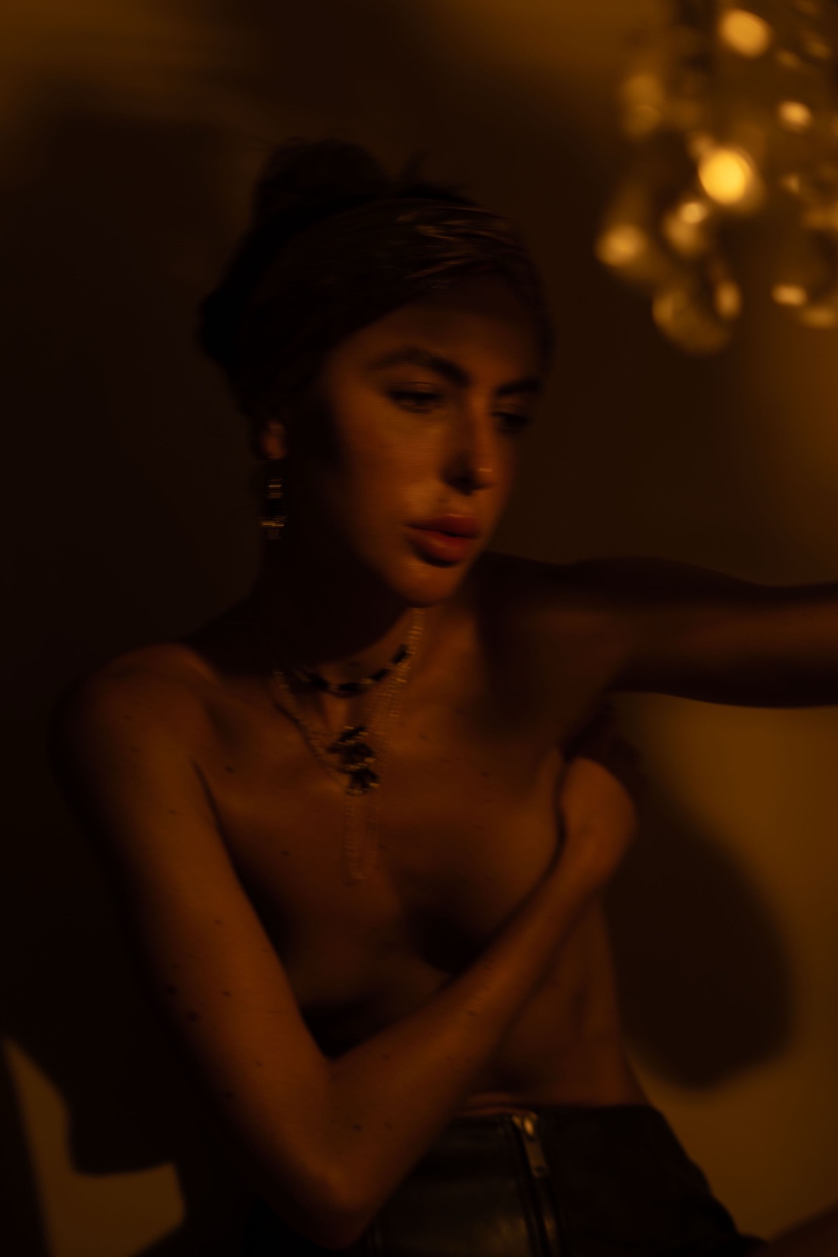 A woman in a gold headwrap turns her shoulder to camera, gold chain necklace at her throat.