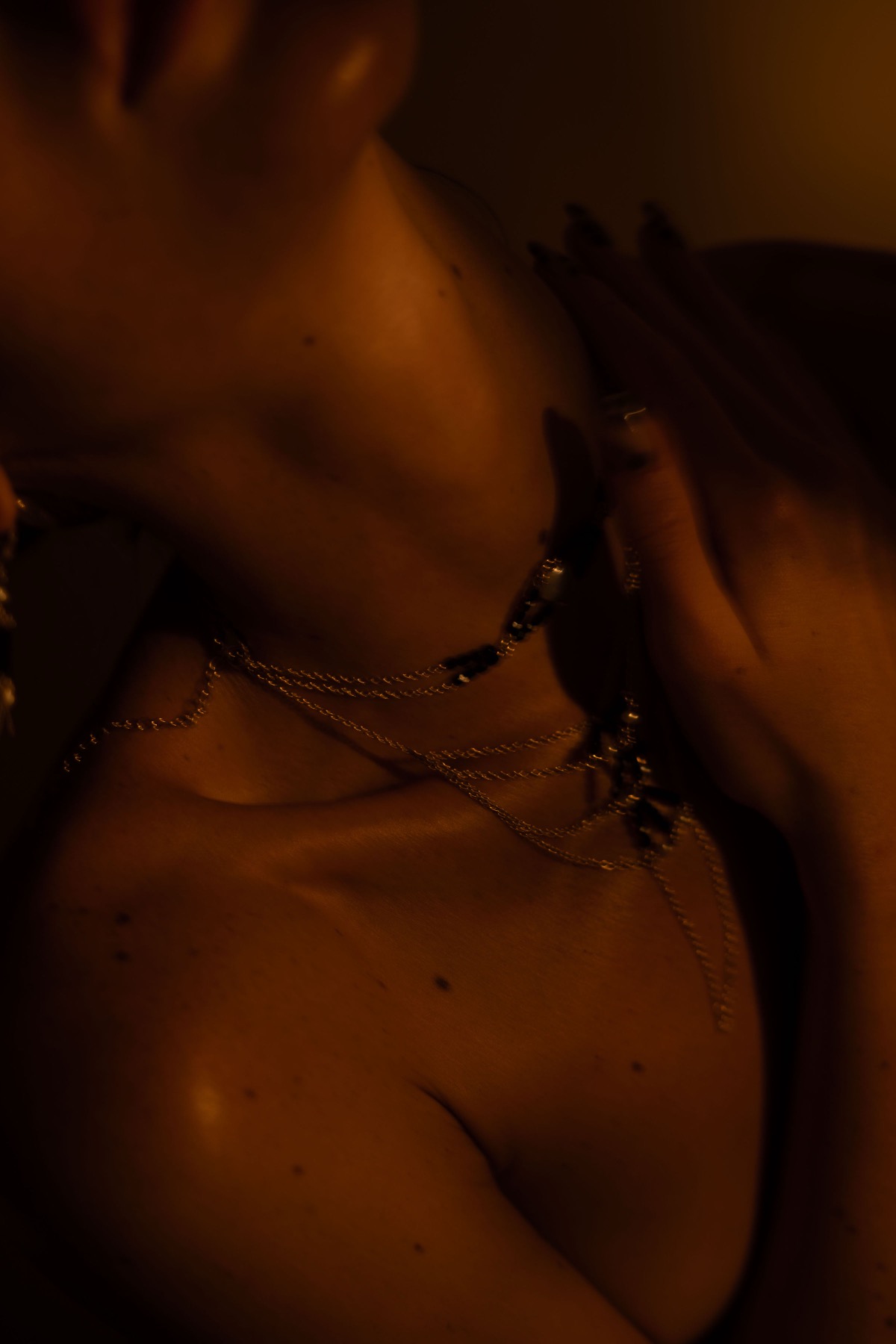 Detail of a fine gold chain necklace with black stones falling across a bare shoulder and collarbone.