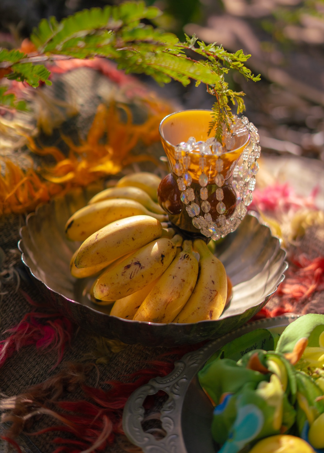 A beaded goblet and a silver dish of bananas among greenery and patterned textiles, styled outdoors in the Riviera Maya.