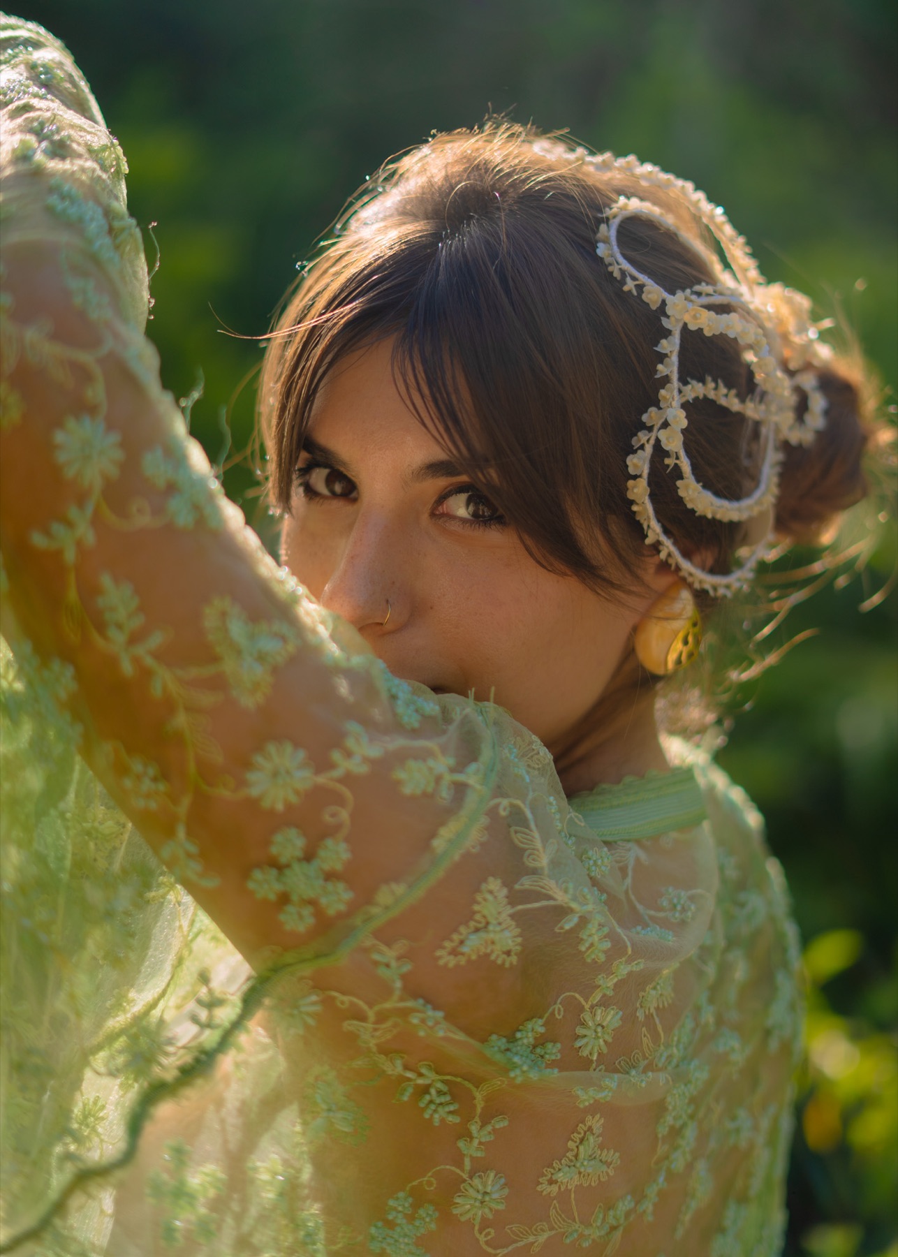 A woman in sheer green lace looks back over her shoulder, pearl headpiece in her hair, Riviera Maya jungle behind her.