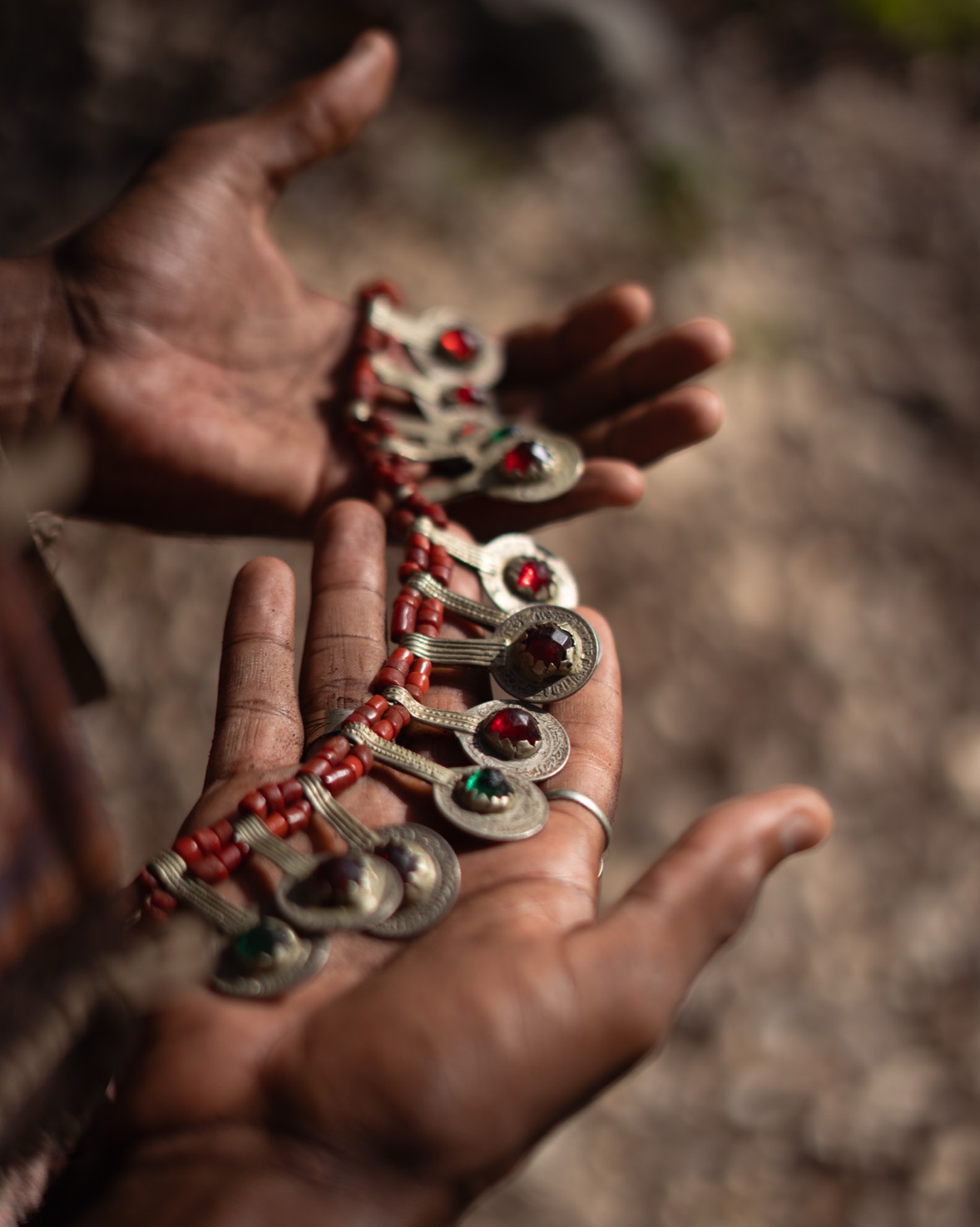 Two cupped hands hold a coral-beaded silver pendant necklace in warm side light.