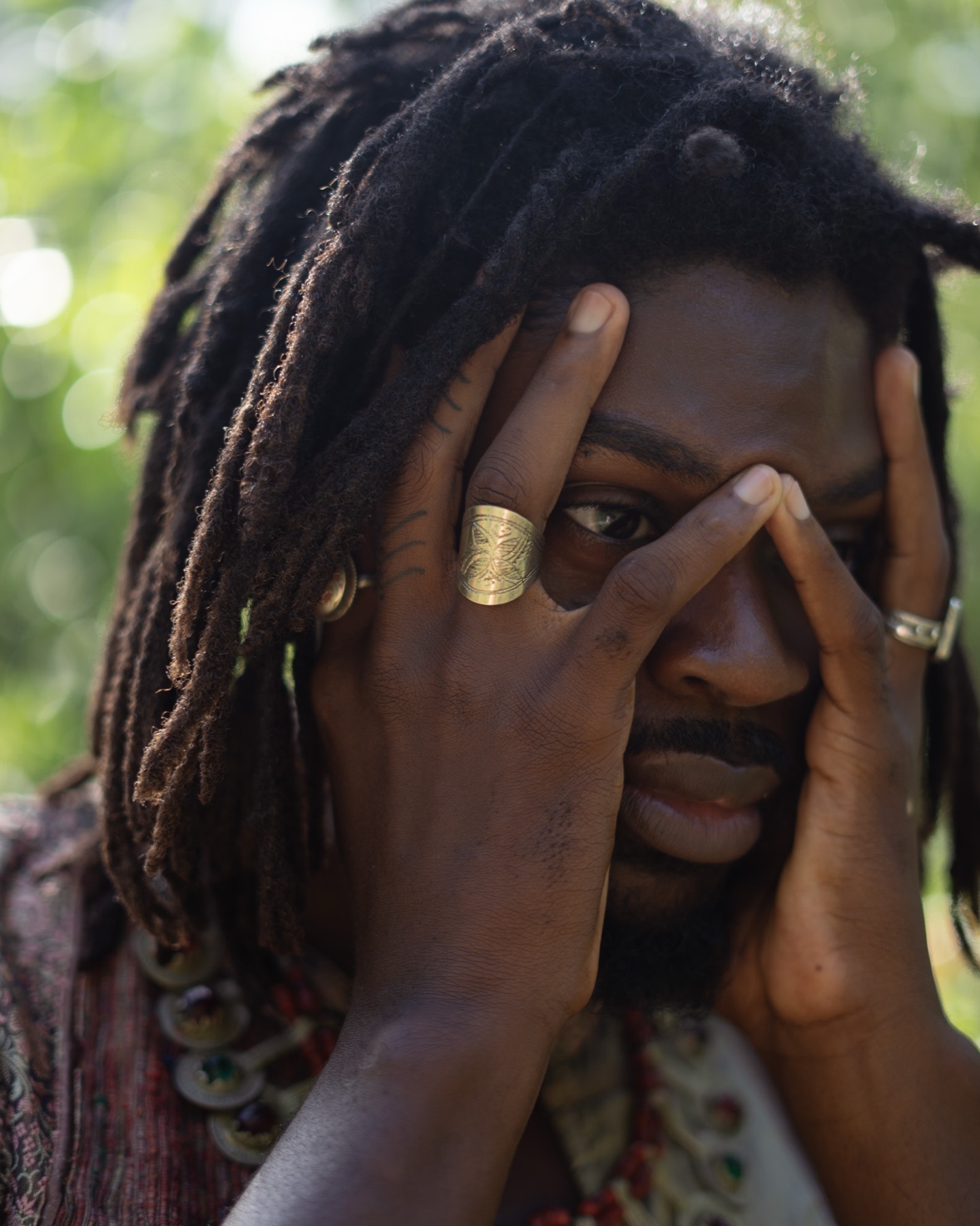 A man presses both hands to his face, a carved gold ring on one finger, one eye visible between them.