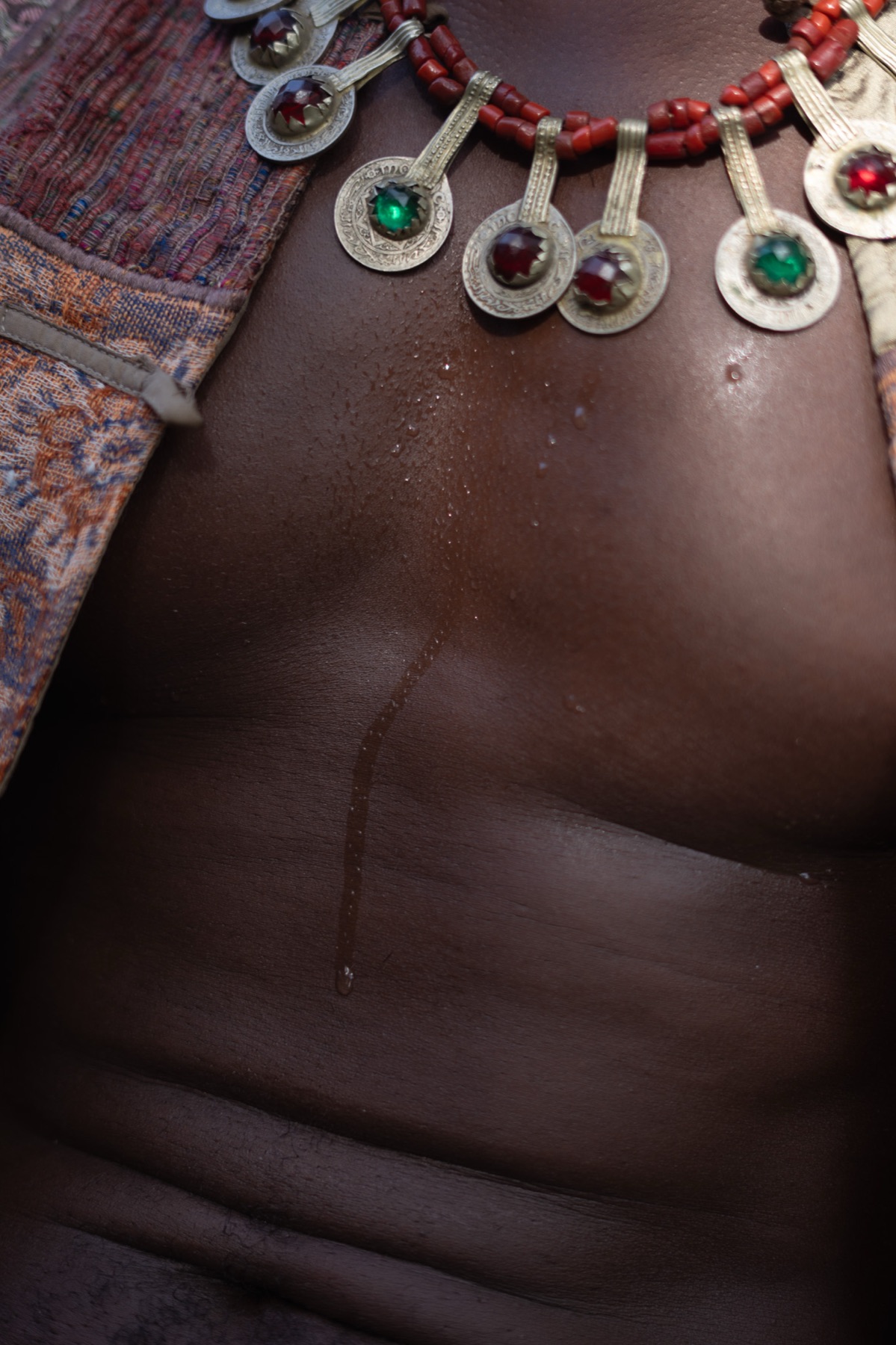 Close frame of a bare torso with a silver and coral collar necklace resting against the skin.