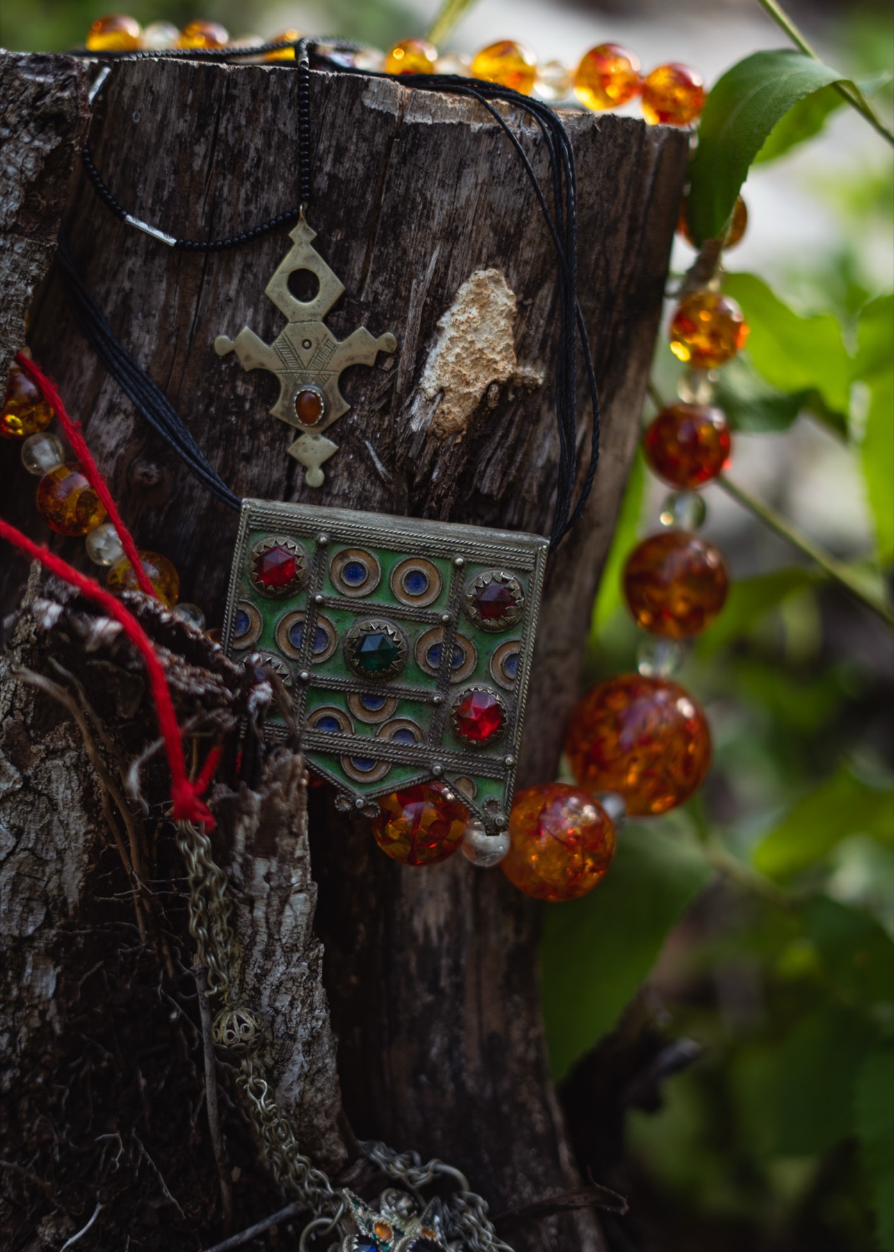 Silver crosses, an enamelled plaque and amber beads hung together on a weathered tree stump.