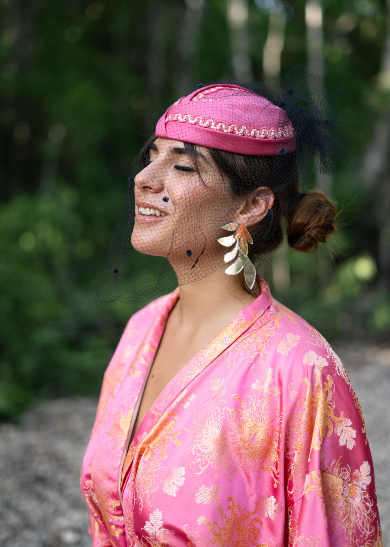 A woman tilts her head back with eyes closed, veil across her face and a silver leaf earring catching the light.