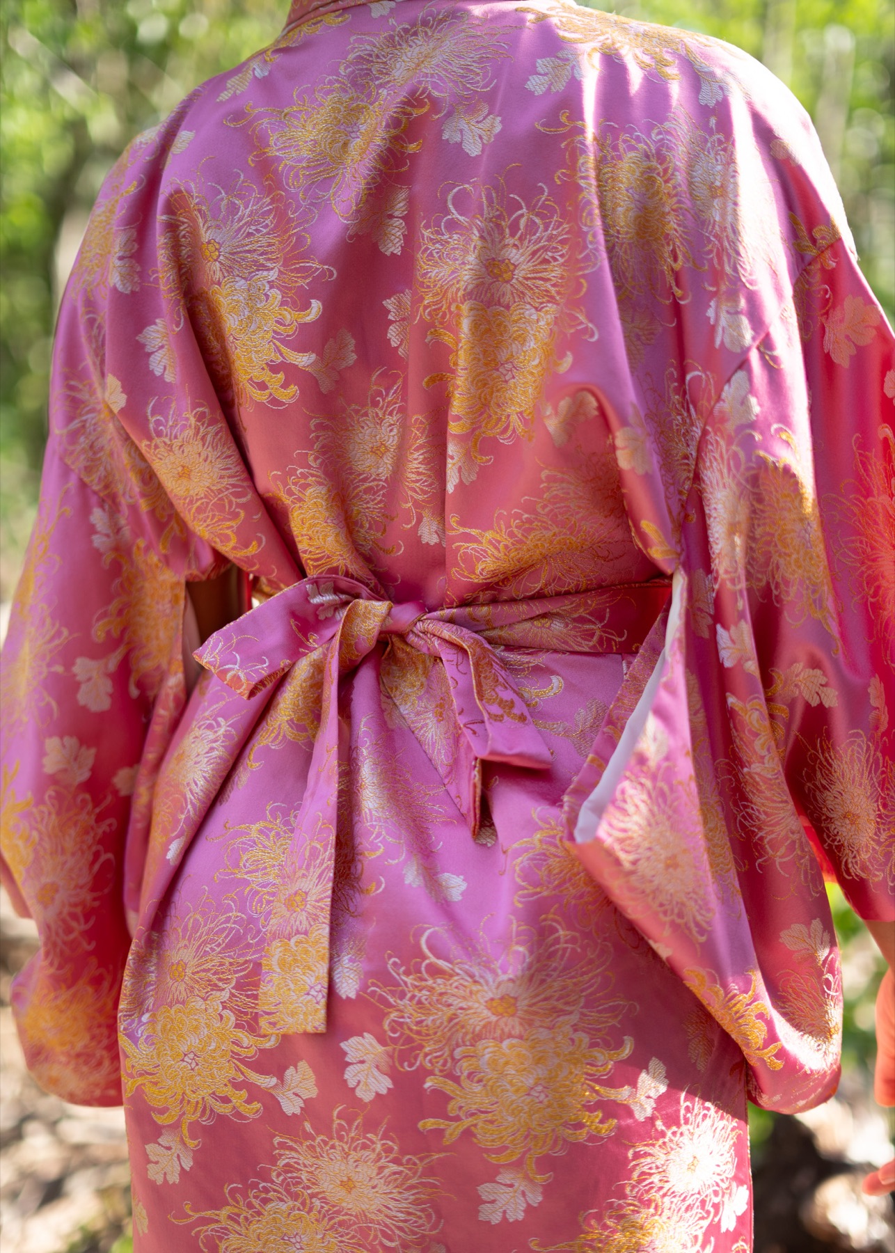 The back of a pink and gold brocade kimono, obi tied in a soft bow at the waist.