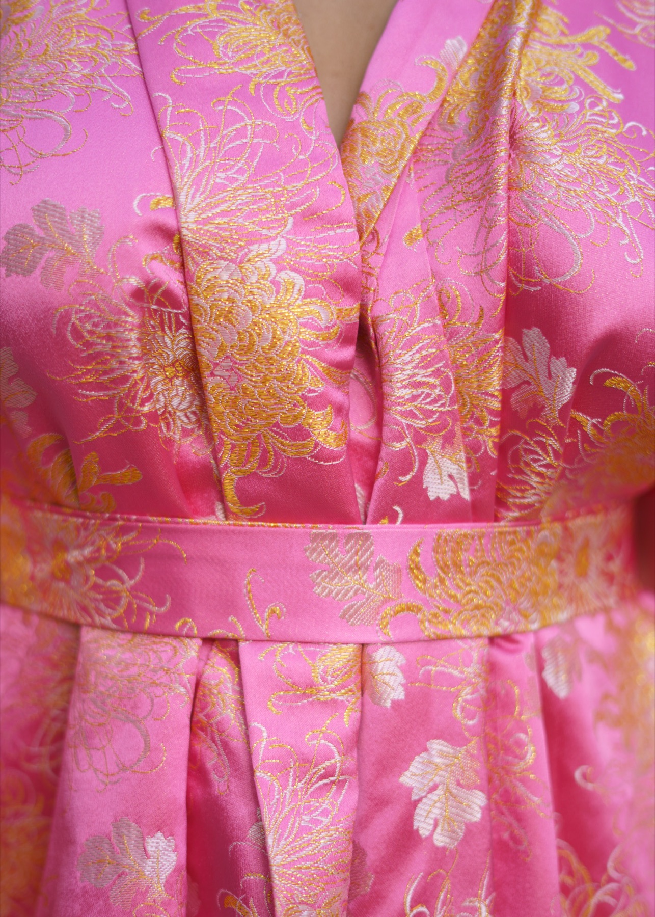 Close detail of the pink brocade kimono's crossed front and tied waist sash, chrysanthemum weave visible.