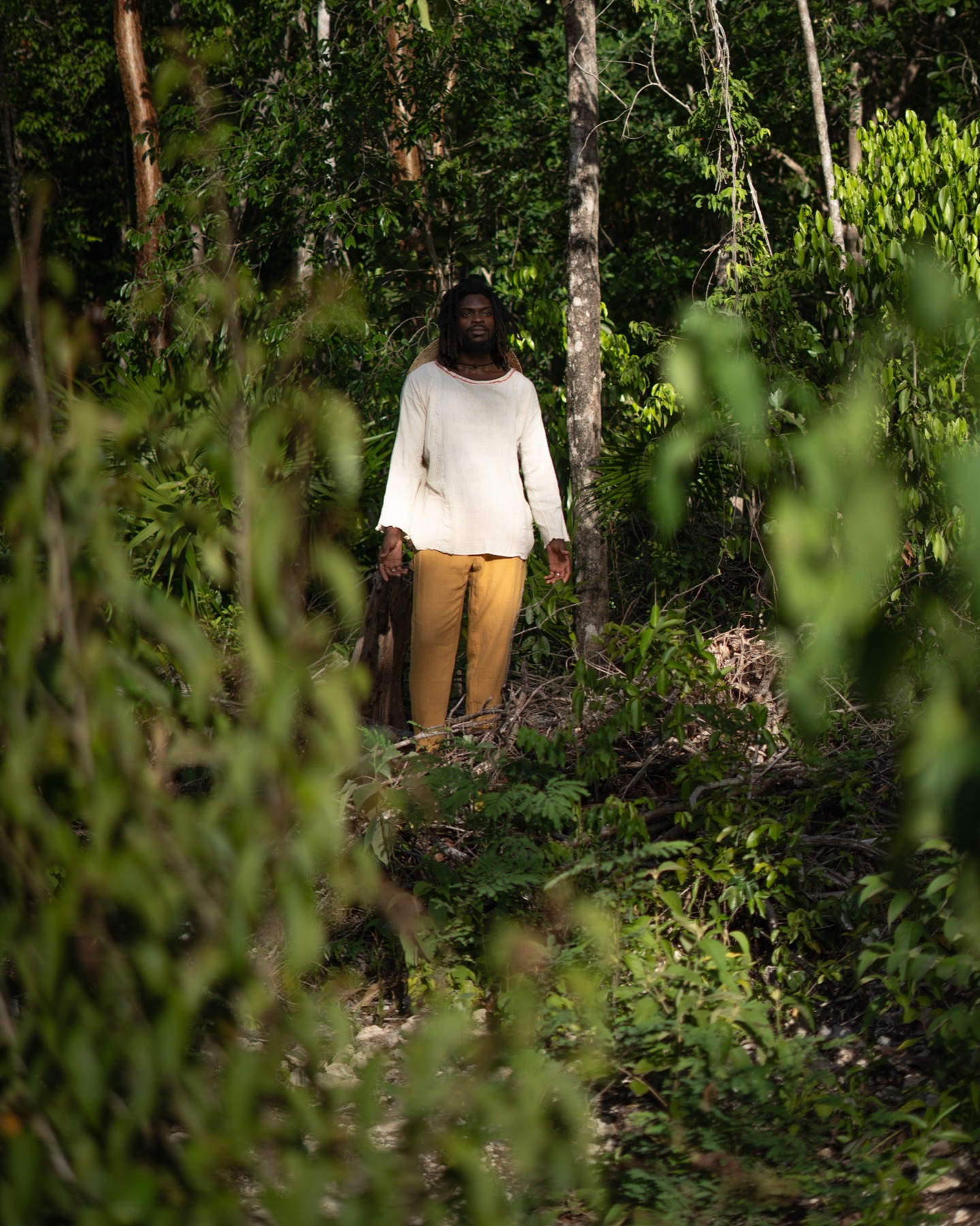 A man stands small and distant in a clearing, framed by out-of-focus jungle leaves.