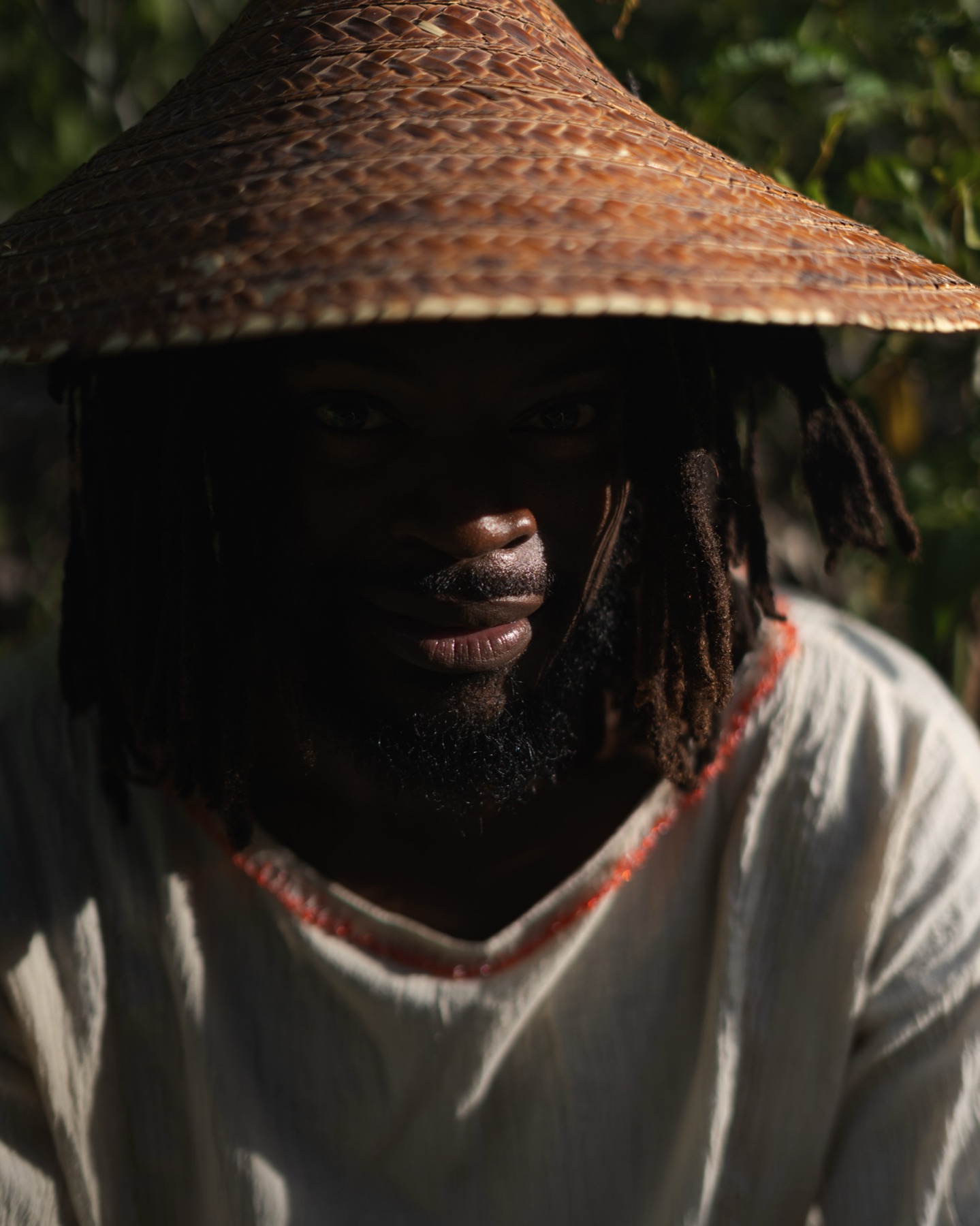 Close portrait of a man under a low straw brim, eyes in shadow, coral-trimmed cream shirt.