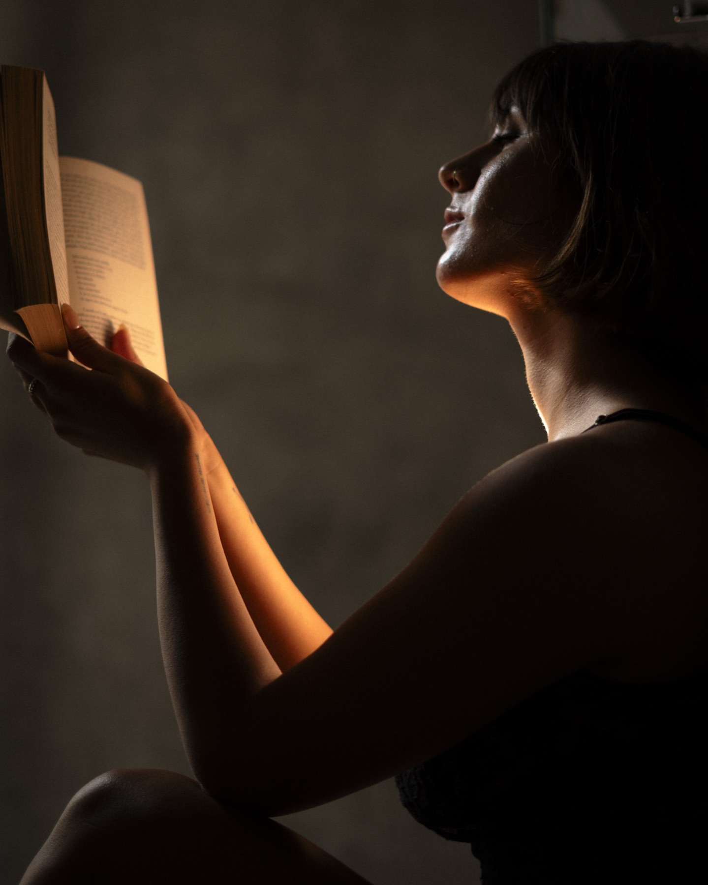 A woman reads a paperback in warm lamplight, the open pages lighting her face and hand.