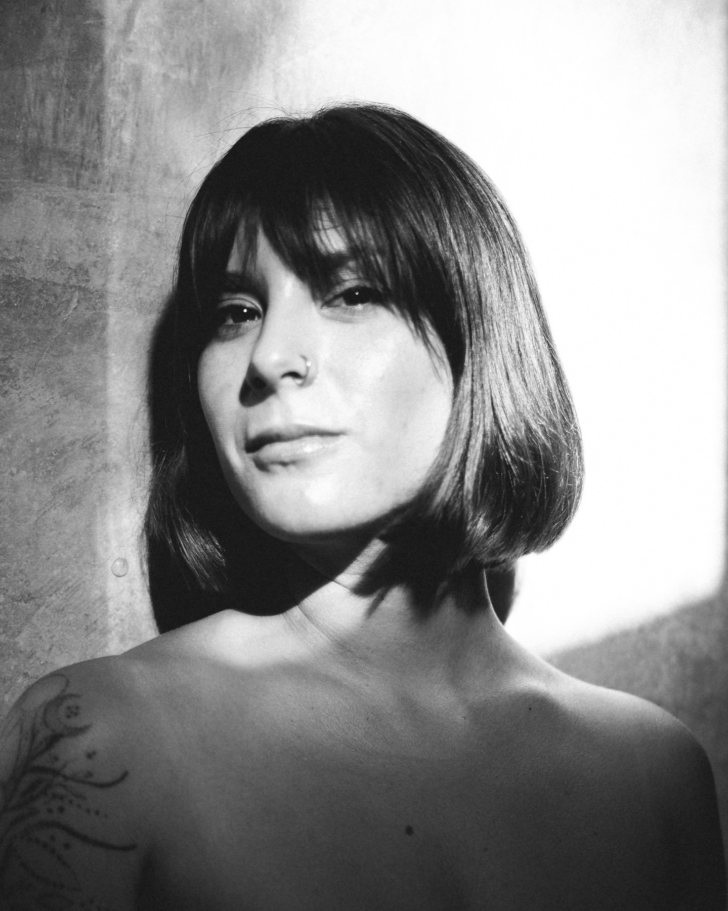 Black and white portrait of a woman with a blunt bob, bare shoulders and a fine line tattoo.