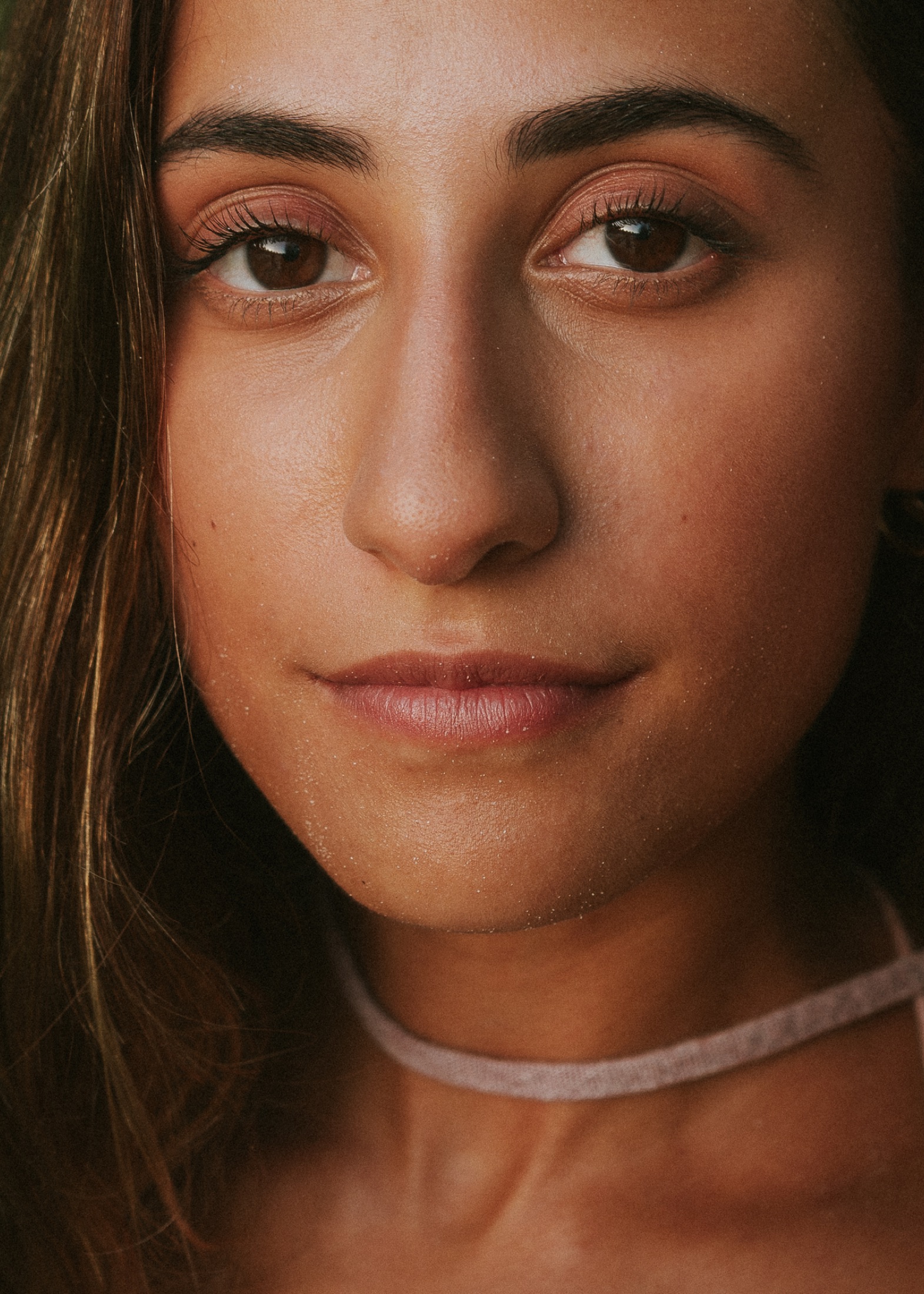 Close portrait of a woman with dark hair and a pale velvet choker, natural light across her face.